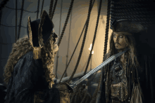 a man in a pirate costume holds a sword and talks to another man