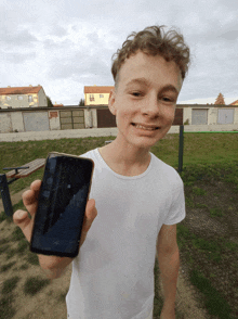 a boy in a white shirt is holding a cell phone in his right hand