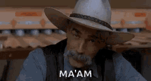 a man with a cowboy hat and mustache is sitting in front of a bowling alley and says ma 'am .