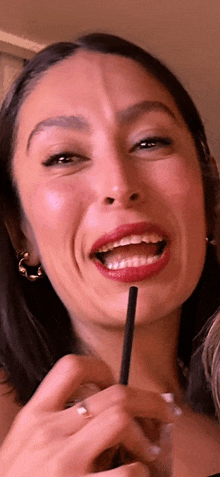 a woman with red lipstick and hoop earrings is holding a straw in her mouth