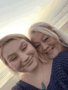 two women are posing for a picture and one has a blue necklace