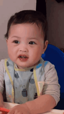 a baby wearing a bib with whales on it is sitting in a blue chair