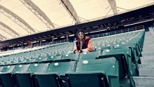 a man sits in an empty stadium with a row of green seats with the numbers 22 and 23 on them