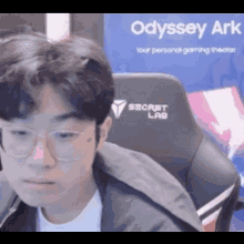 a man wearing glasses is sitting in front of an odyssey ark advertisement