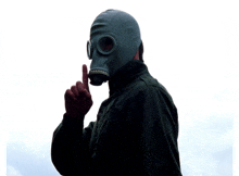 a man wearing a gas mask has his finger on his lips