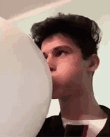 a young man is blowing up a white balloon in his mouth .