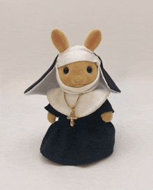 a stuffed bunny is dressed as a nun and has a cross necklace around her neck