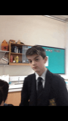 a boy in a suit and tie stands in front of a blue board that says the wall