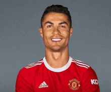 a man wearing a red adidas manchester united jersey smiles for the camera