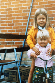 a little girl is riding a tricycle next to a box that says pizza on it