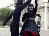 a man in a top hat and a woman in a black dress are dancing in front of a building