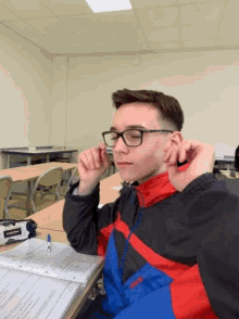 a young man wearing glasses and a jacket with the word columbia on it sits at a desk in a classroom