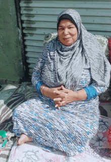 a woman wearing a hijab sits on a blanket