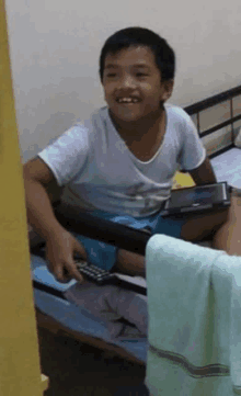 a young boy is sitting on a bed holding a remote control .