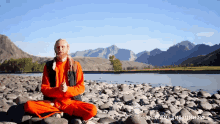 a man sits on rocks near a river with mountains in the background and the words " урокмедитации.рф " below him