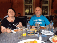 a man wearing a blue shirt that says gio paoli sits at a table