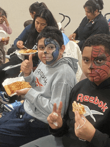 a boy with spiderman painted on his face eating pizza