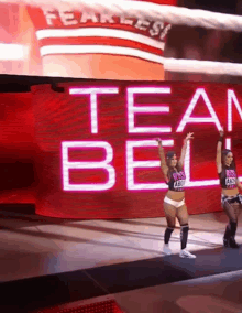 two female wrestlers are dancing in front of a large screen that says team bell