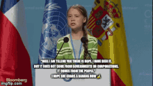 a girl is giving a speech in front of a podium with flags behind her and a quote from bloomberg