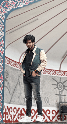 a young man in a jacket stands in front of a wall with a border that says ' x ' on it