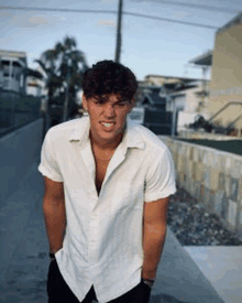 a young man in a white shirt is standing on a sidewalk with his hands in his pockets .