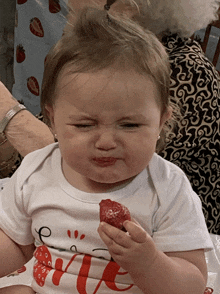 a baby wearing a shirt that says " me " eating a strawberry