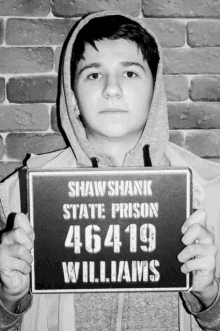 a man in a hoodie is holding up a sign that says shaw shanic state prison 46 419 williams