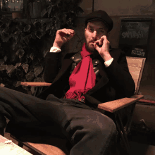 a man in a black jacket and red scarf is sitting in a chair in front of a sign that says hello rock