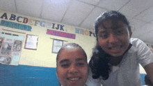 two girls are posing for a picture in front of a wall with the alphabet