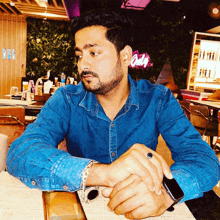 a man in a blue shirt is sitting at a table in front of a neon sign that says owls