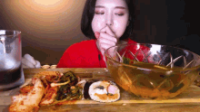 a woman in a red shirt is sitting at a table with a bowl of soup and a plate of food .