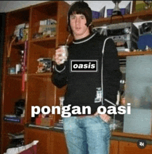 a man wearing a sweater with the word oasis on it is holding a cup of coffee .