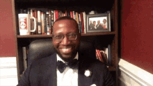 a man in a tuxedo sits in front of a bookshelf with a picture of a man in a tuxedo on it