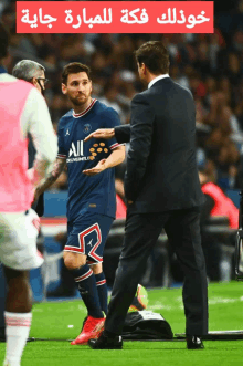 a man in a suit talks to a soccer player who is wearing a jersey that says all