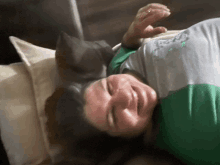 a woman in a green and grey shirt is smiling while laying on a bed