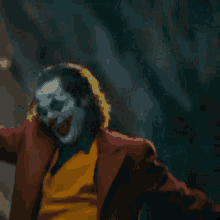 the joker is wearing a clown mask and a red suit and is dancing in a dark room .