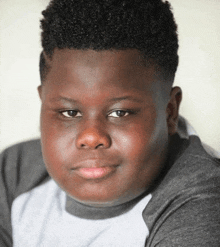 a young boy with curly hair is wearing a gray shirt and looking at the camera