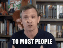 a man is standing in front of a bookshelf with the words to most people written on his face .