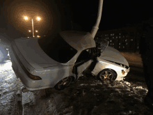 a white car that has crashed into a pole with the hood open