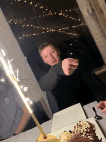 a man is pointing at a cake with a sparkler on it