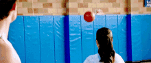 a man and a woman are playing volleyball in front of a blue wall with a sign that says ' basketball ' on it