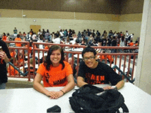 two people sitting at a table with one wearing an orange shirt that says " women "