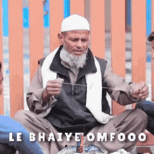 a man with a beard is sitting in front of a wooden fence with the words le bhaiye omfood written on the bottom