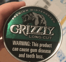 a person is holding a can of grizzly long cut premium wintergreen