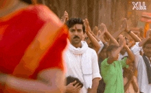 a man in a white shirt stands in front of a crowd of people with their hands in the air