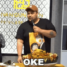 a man is holding a microphone in front of a plate of food with the word oke on it .