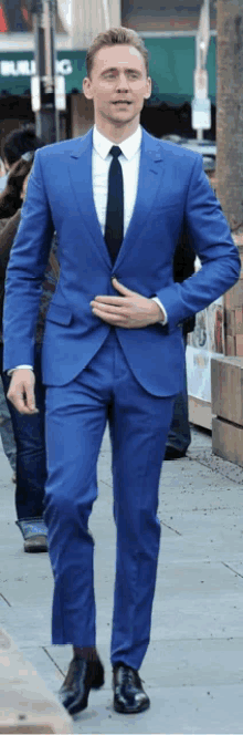 a man in a blue suit and black tie is walking down a sidewalk