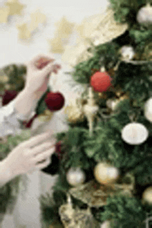 a person is decorating a christmas tree with balls and decorations .