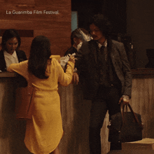 a woman in a yellow dress stands next to a man in a suit at a la guarimba film festival reception desk