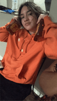 a girl in an orange nike hoodie holds a bottle